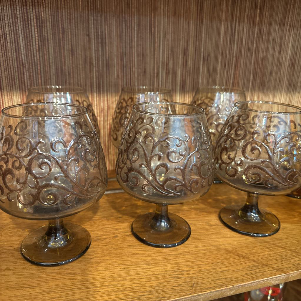 Set of ornate glass goblets on a wooden surface with a wooden panel background.