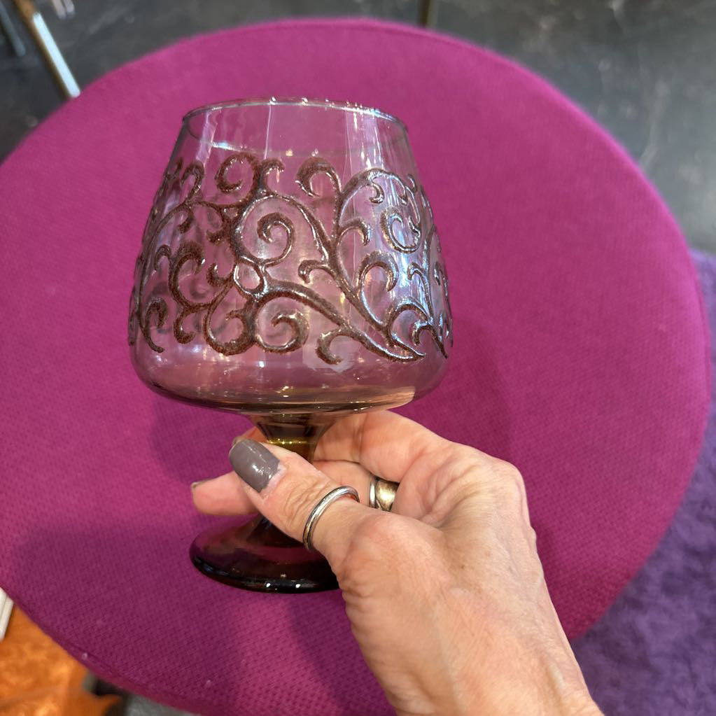 Hand holding a decorative glass against a purple cushioned chair