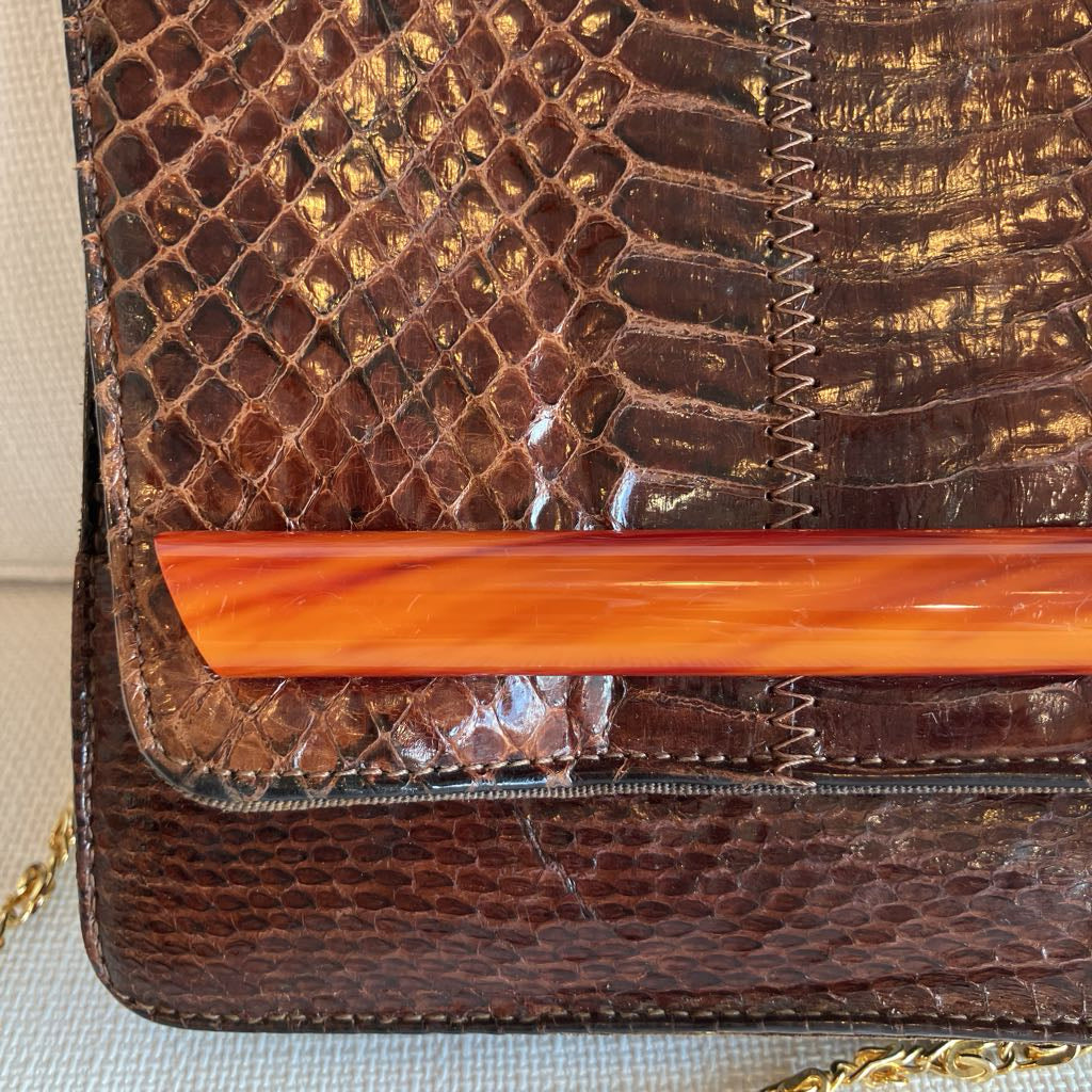 Close-up of a brown textured clutch with an orange handle.