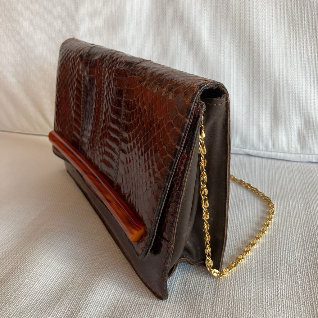 Brown crocodile-patterned clutch bag with a gold chain on a light background