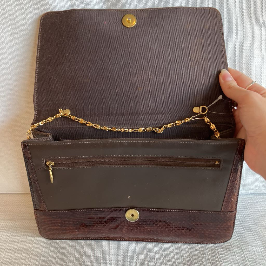 Brown leather handbag with gold chain and clasp on a light background