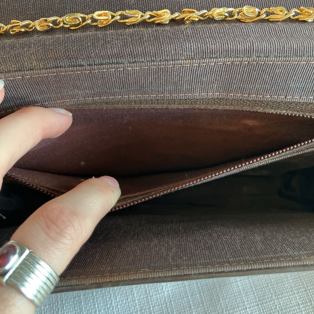 Brown handbag with gold chain handle held by a hand wearing a silver ring.