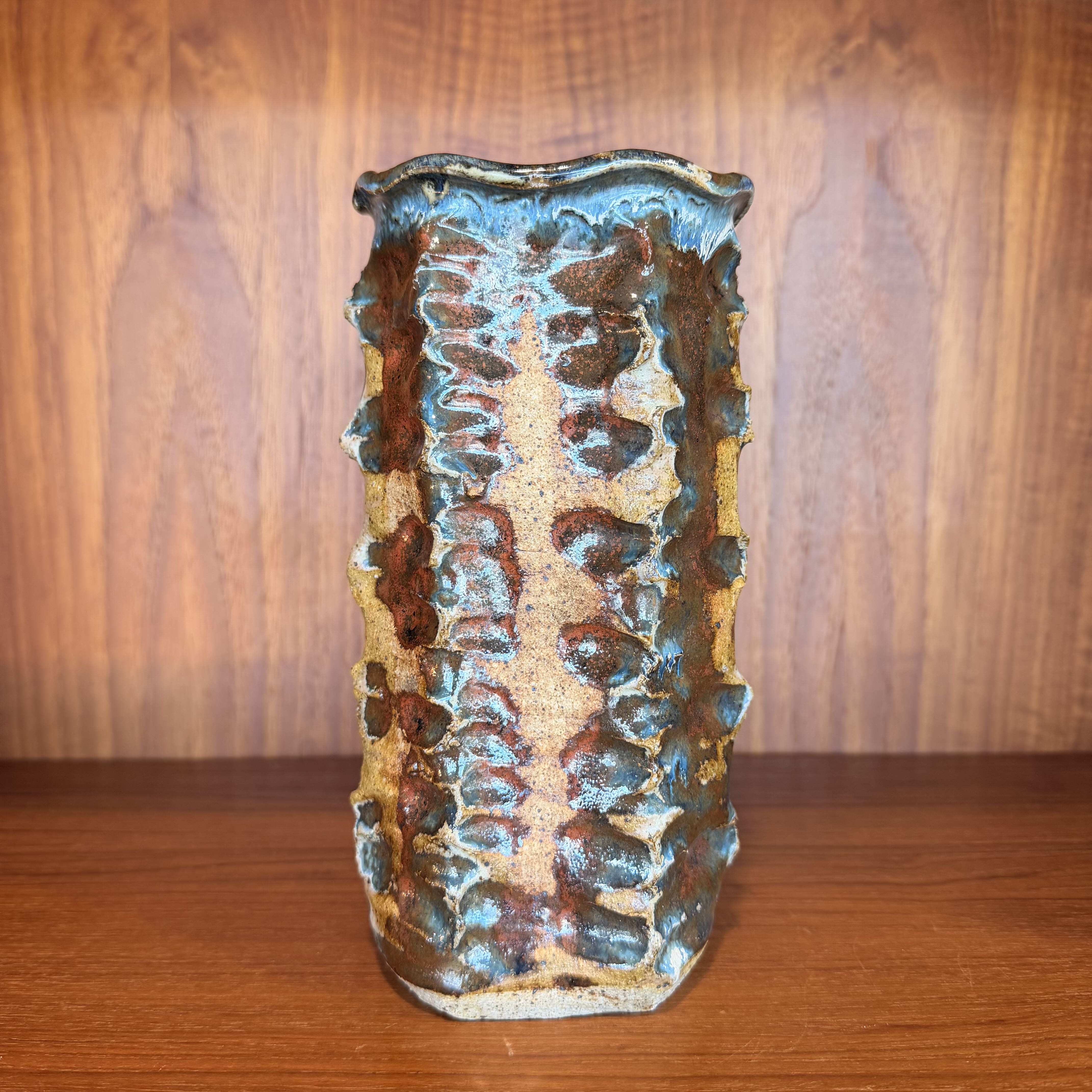 Textured ceramic vase on a wooden surface with a wooden background