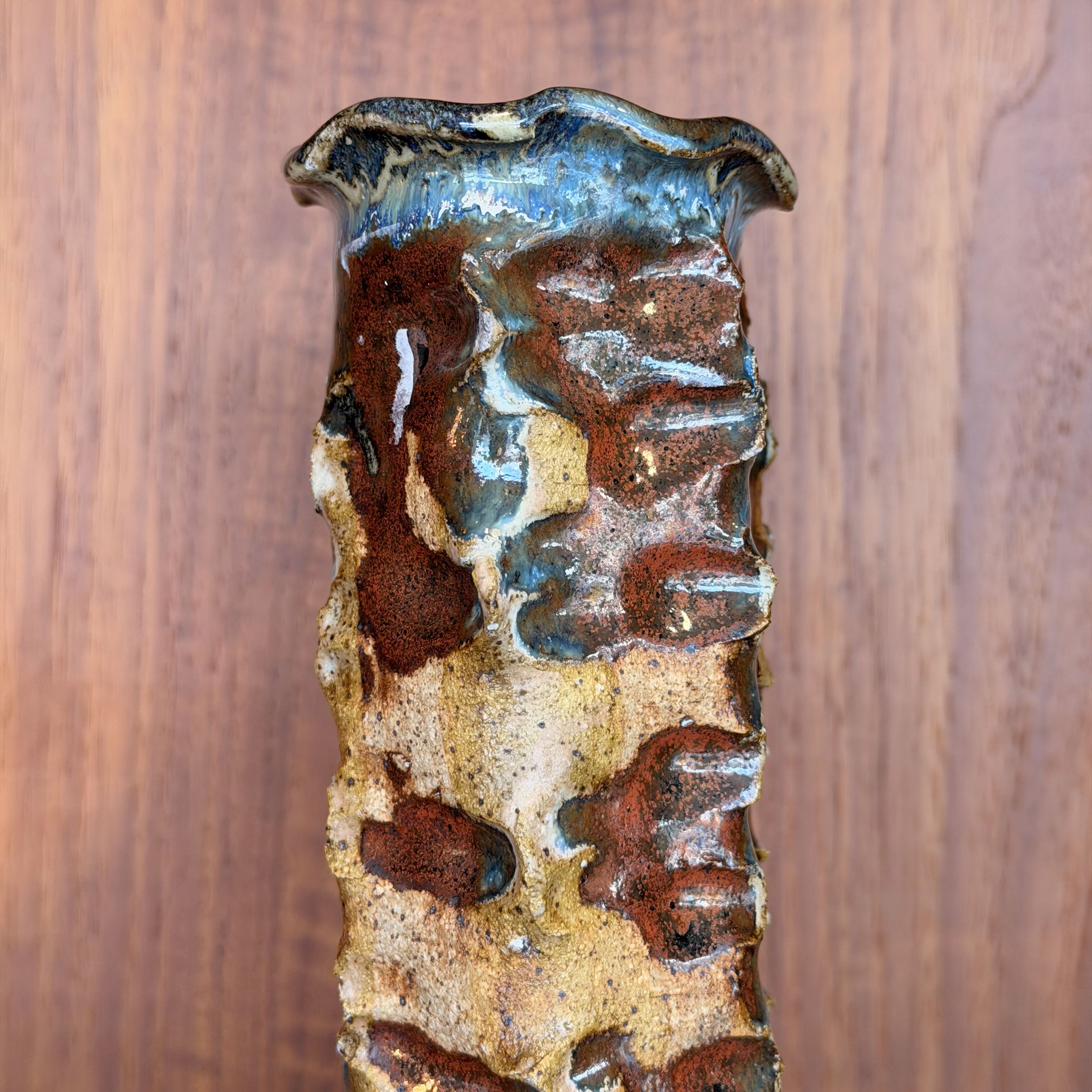 Textured ceramic vase with brown and blue glaze on a wooden background