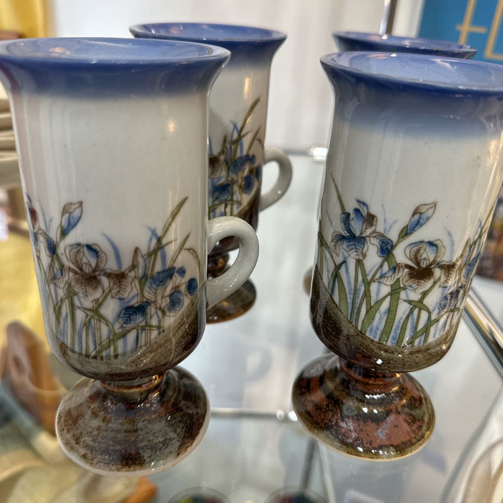Set of four ceramic cups with floral designs on a reflective surface