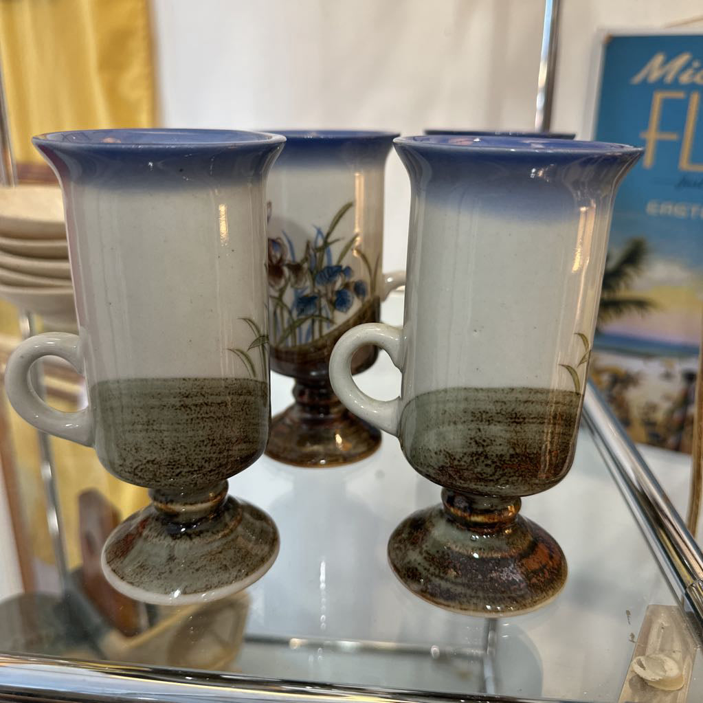 Set of three ceramic cups with handles on a reflective surface