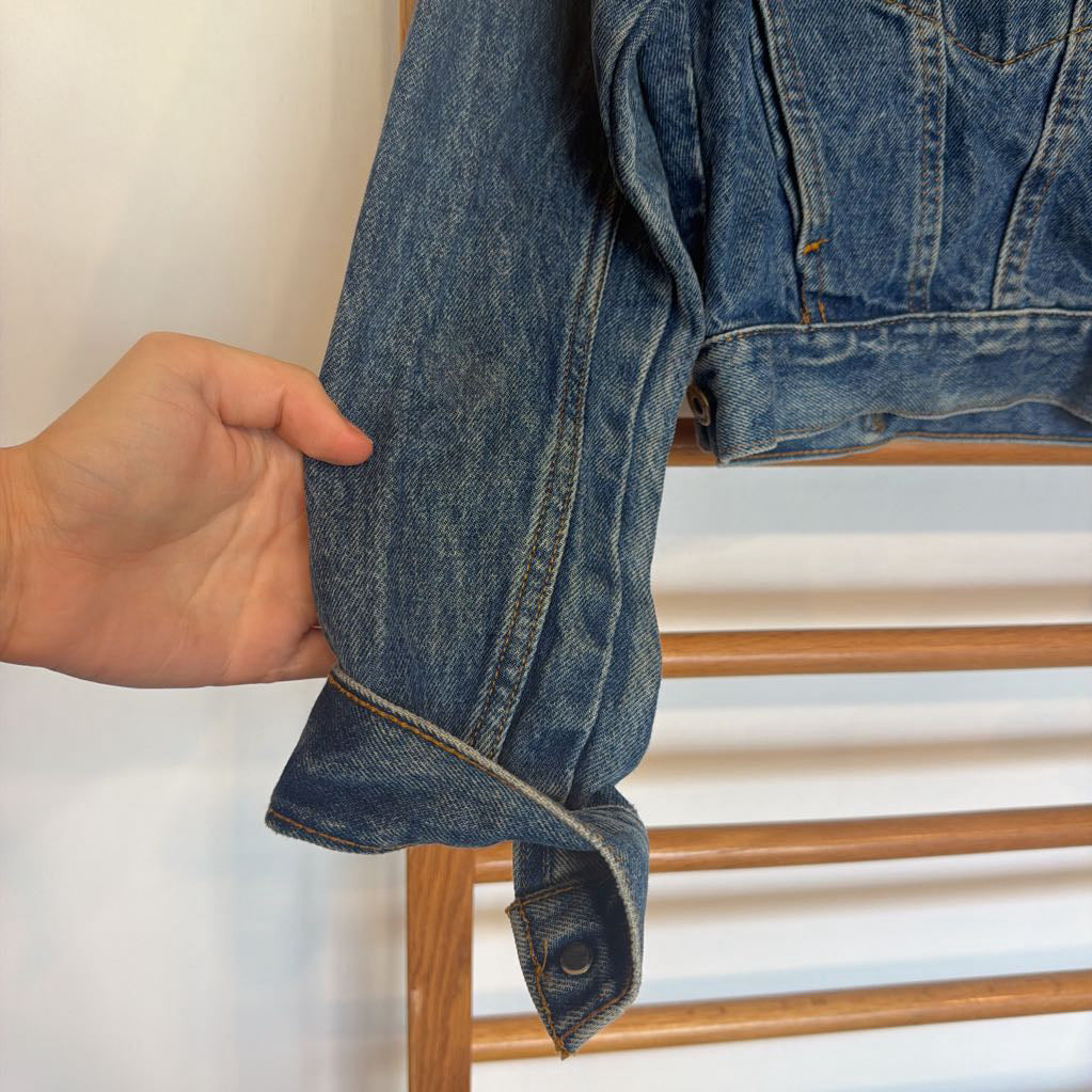 Hand holding a blue denim jacket against a neutral background