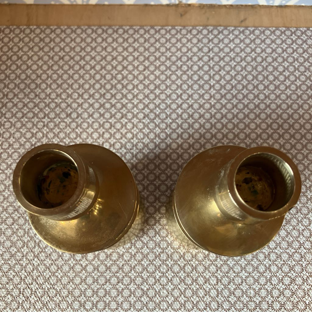Two brass candle holders on a patterned fabric background