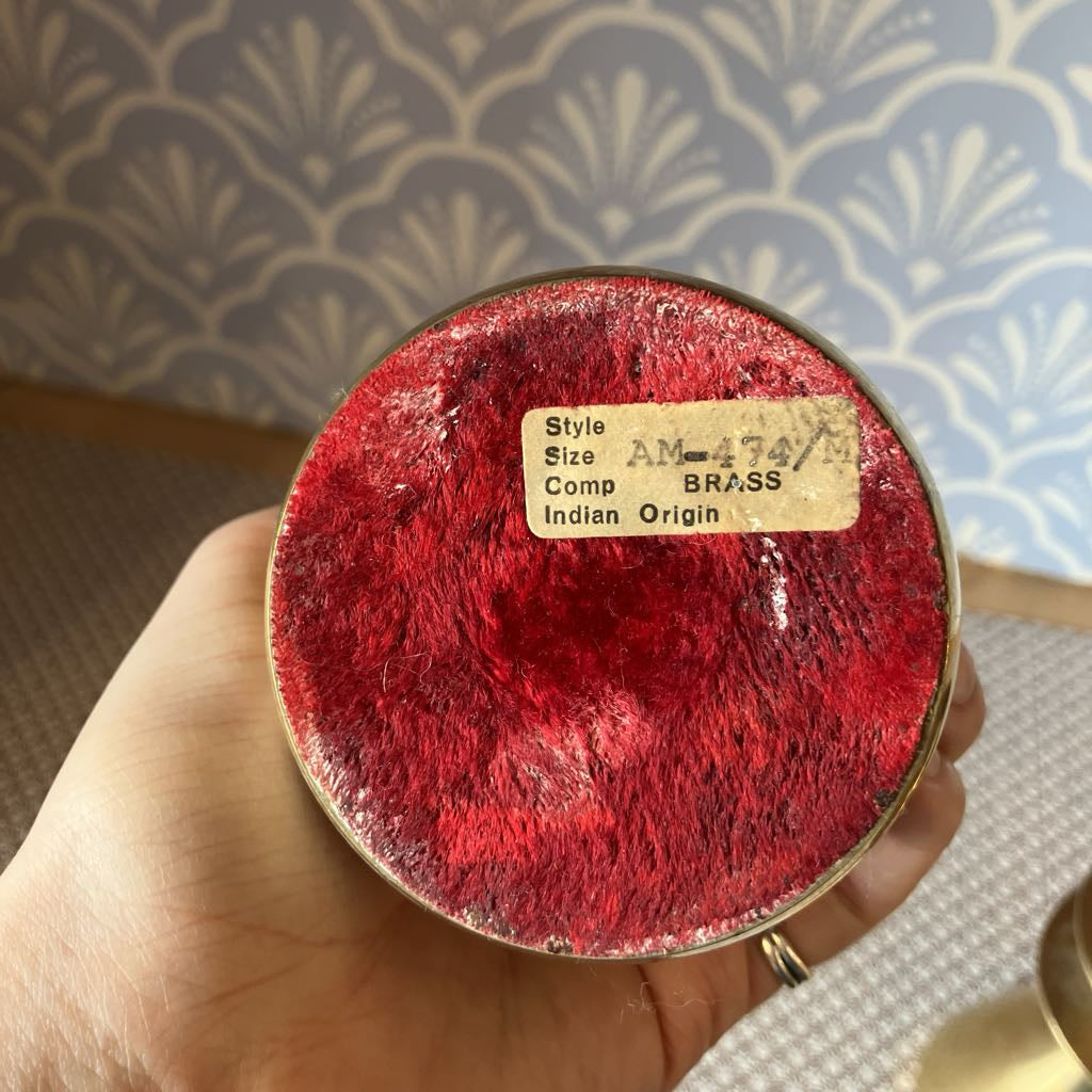 Round red object with a label held by a hand against a patterned wall.