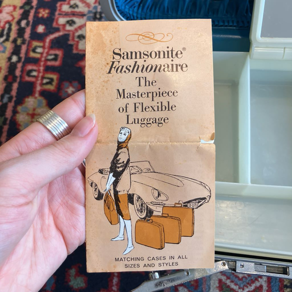 Samsonite Fashionaire luggage brochure held by a hand with a suitcase in the background.