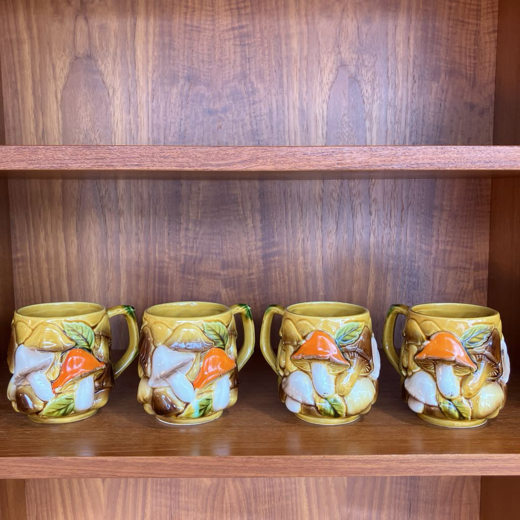 Four ceramic mugs with decorative designs on a wooden shelf