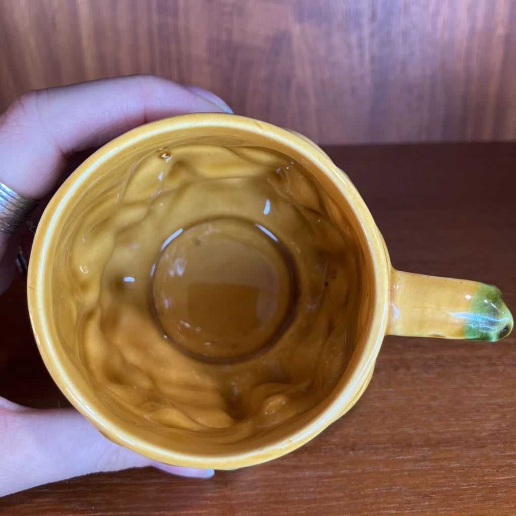 Yellow mug with wavy design held by a hand on a wooden surface