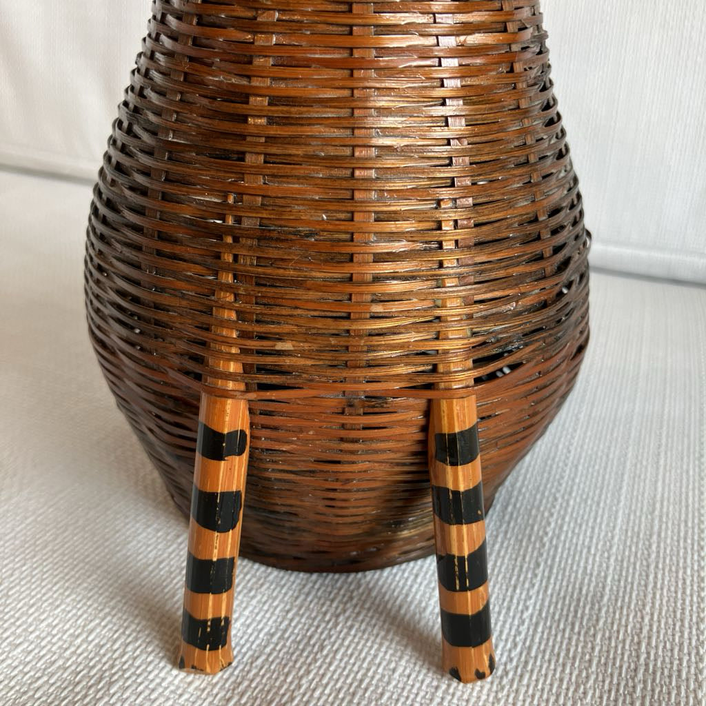 Wicker basket with black and brown striped legs on a light background