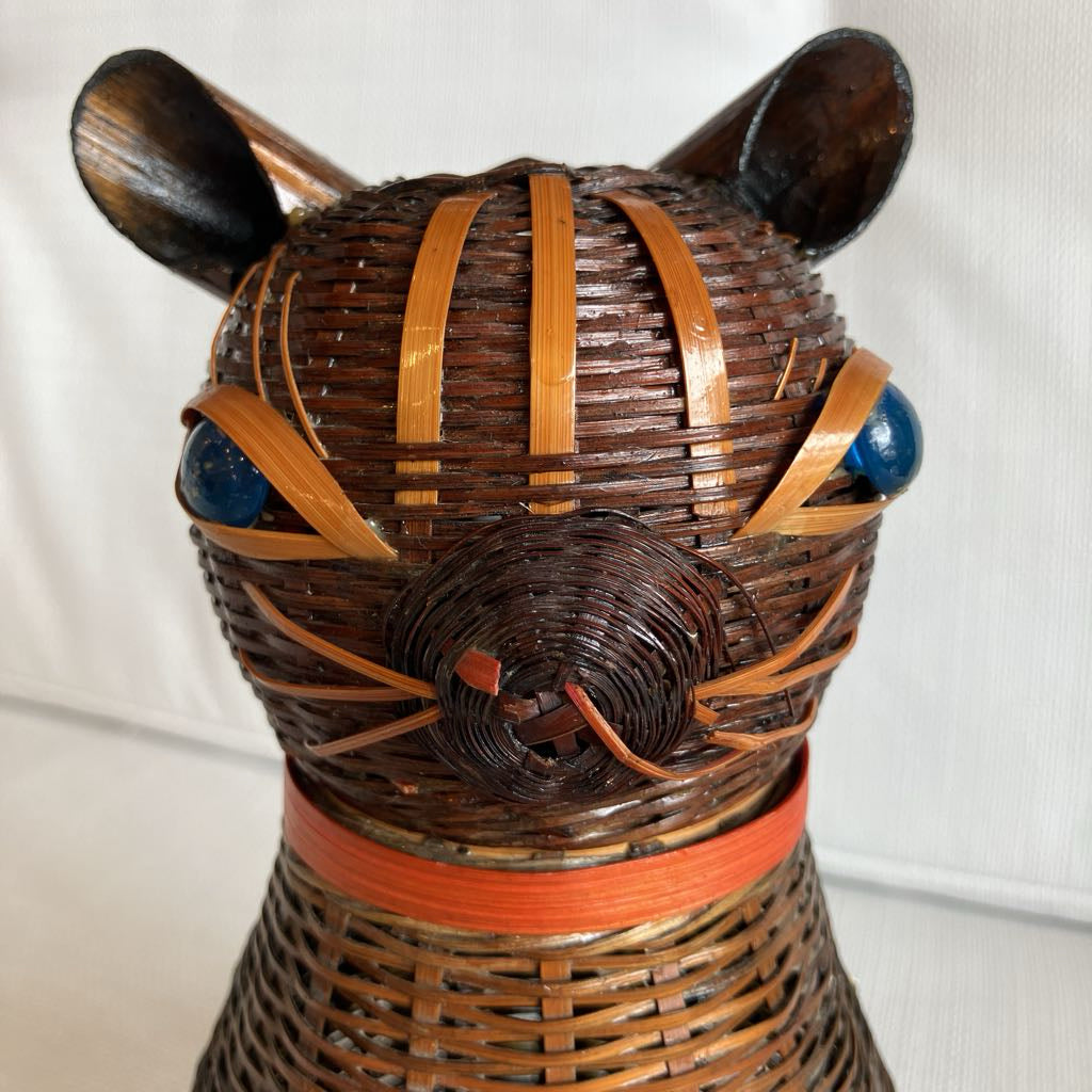Wicker cat-shaped decorative item with wooden ears and blue eyes on a white background
