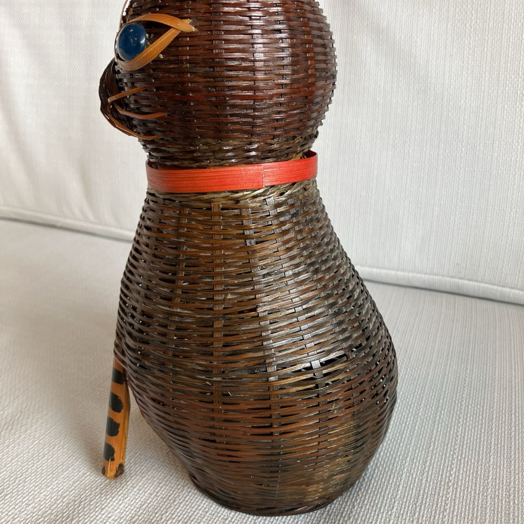 Wicker cat-shaped object with a red band around its neck on a white surface