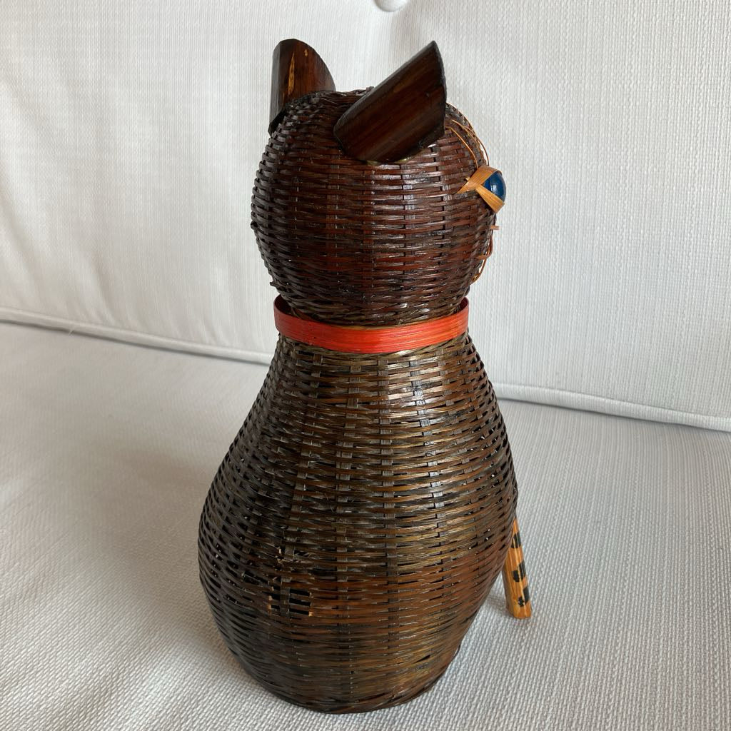 Wicker cat-shaped object with a red ribbon on a light background