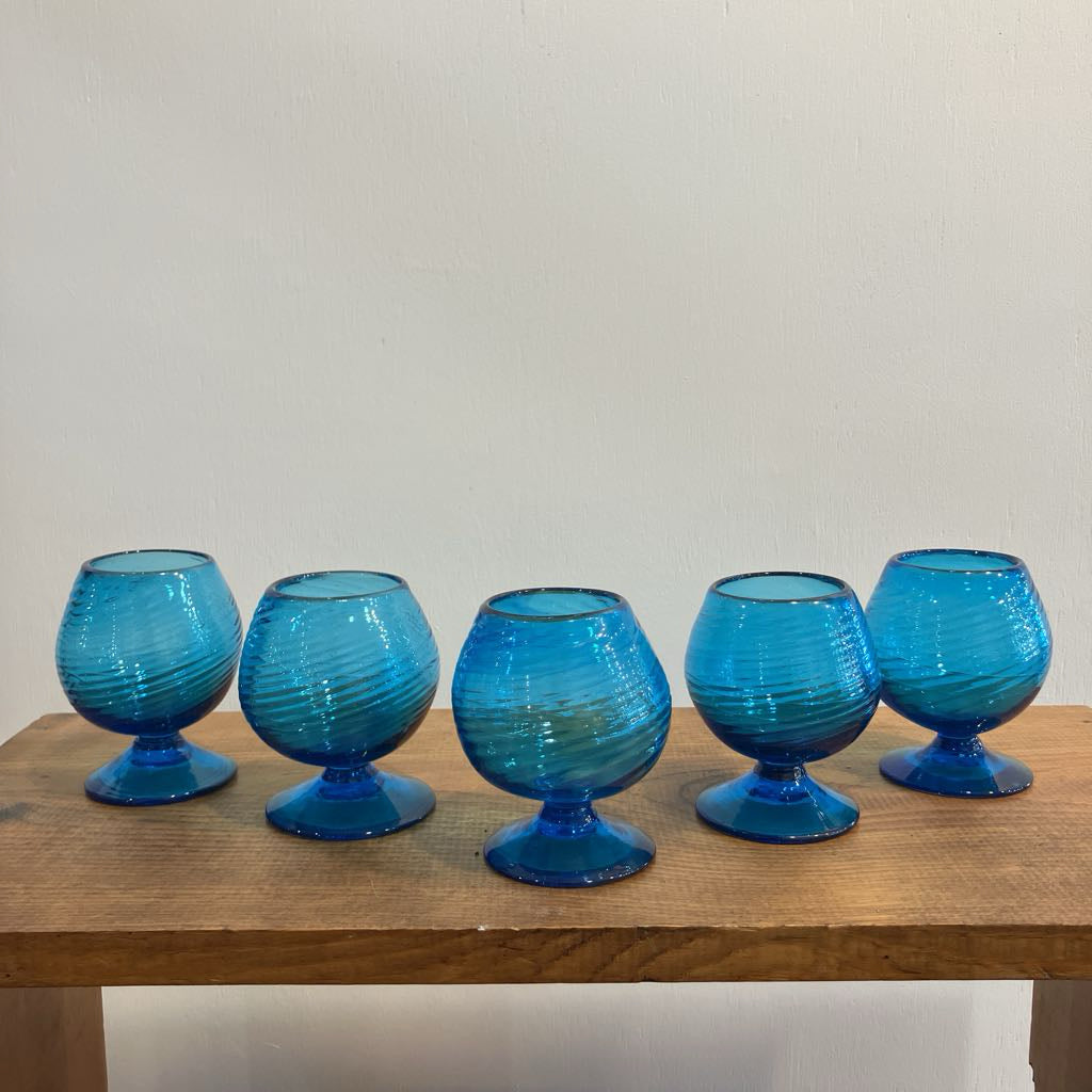 Five blue glass tumblers on a wooden surface with a plain background