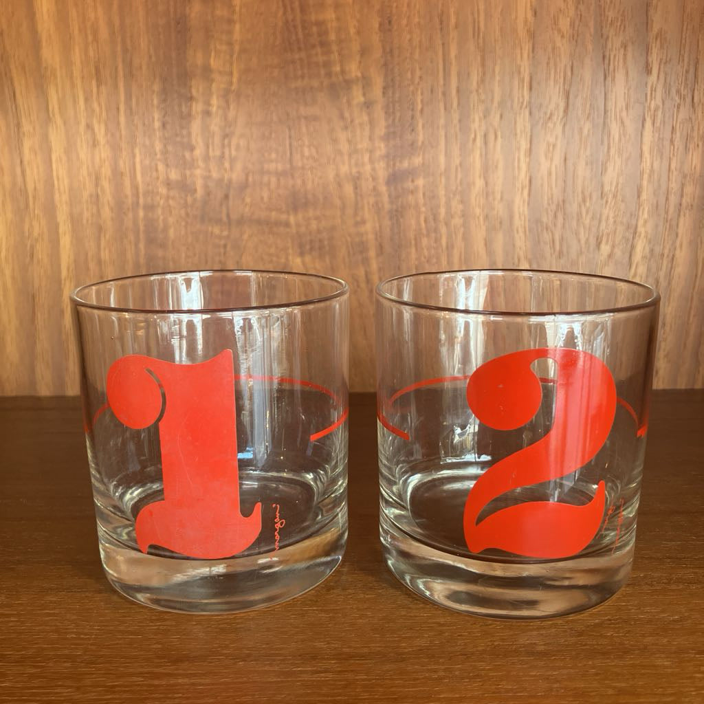 Two clear glasses with red numbers '1' and '2' on a wooden surface.