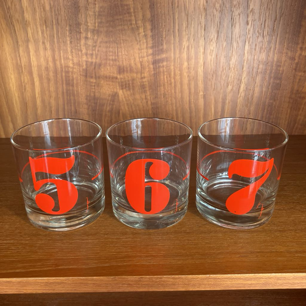 Three clear glasses with red numbers "5, 6, 7" on a wooden surface