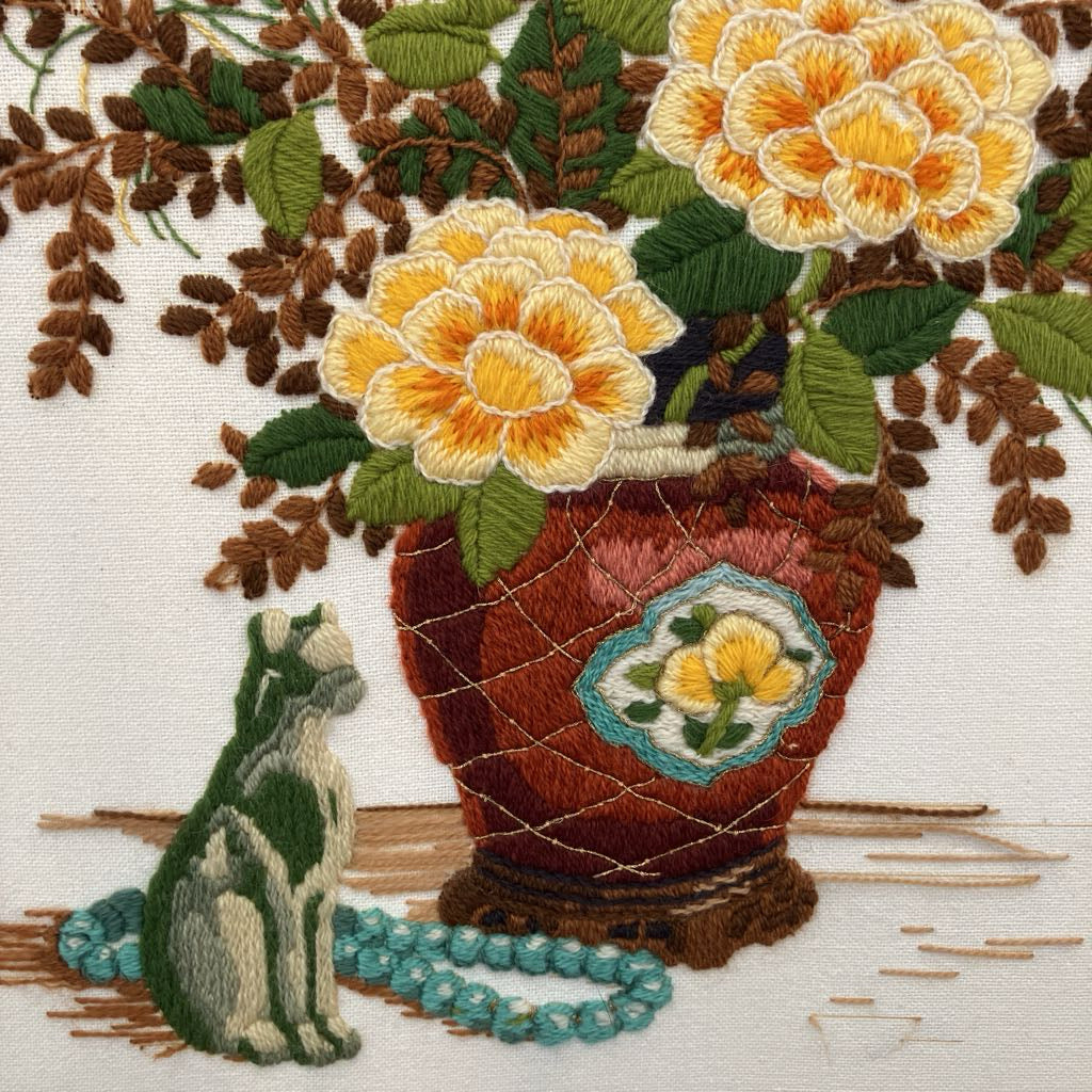Embroidered design of a cat sitting next to a vase with flowers