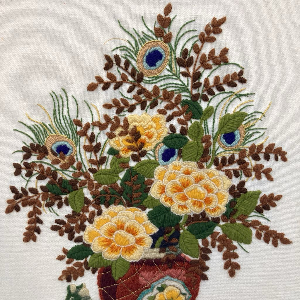 Embroidered design of flowers and peacock feathers on a white background