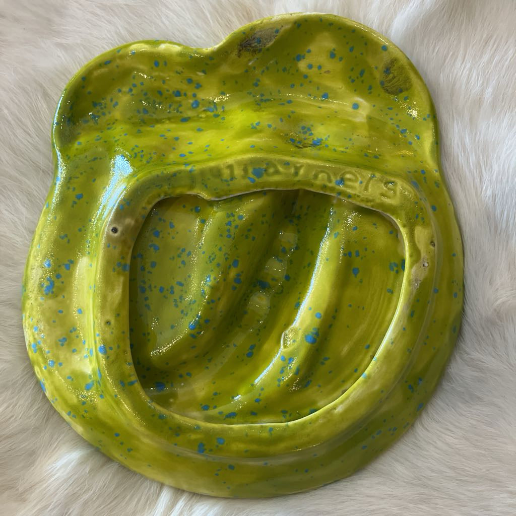The bottom of a green ceramic dish with blue specks on a light wooden surface