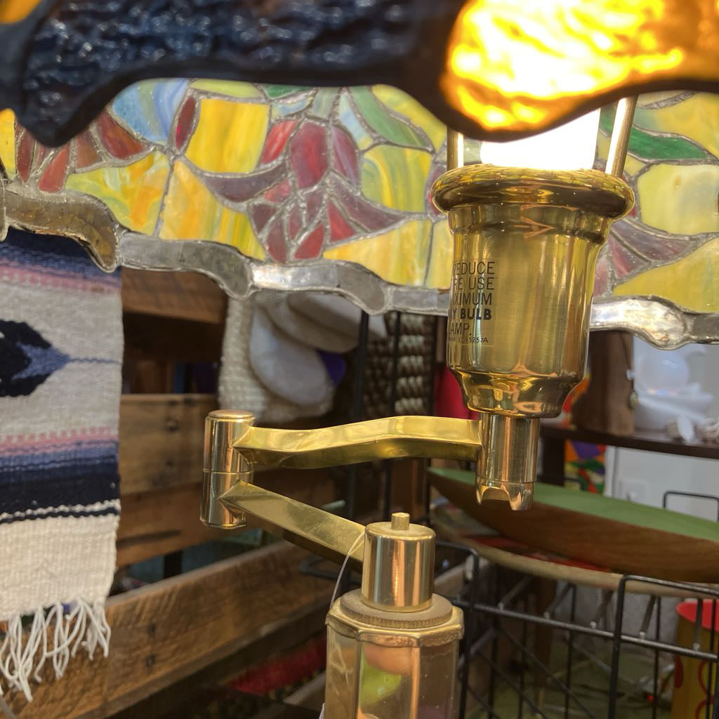 Vintage-style lamp with stained glass shade and brass arm in a cozy room setting.