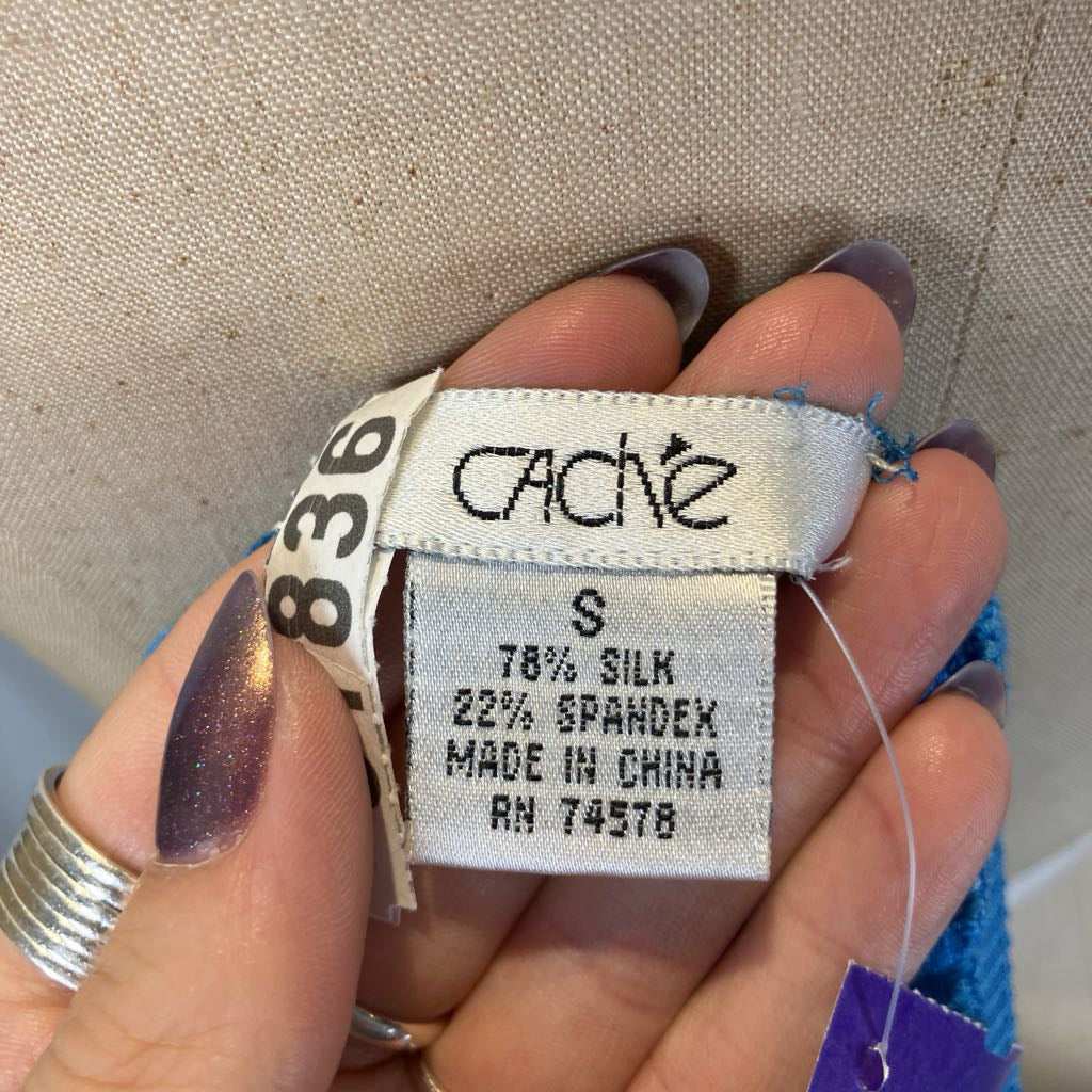 Close-up of a fabric label with 'cache' branding held by a hand.