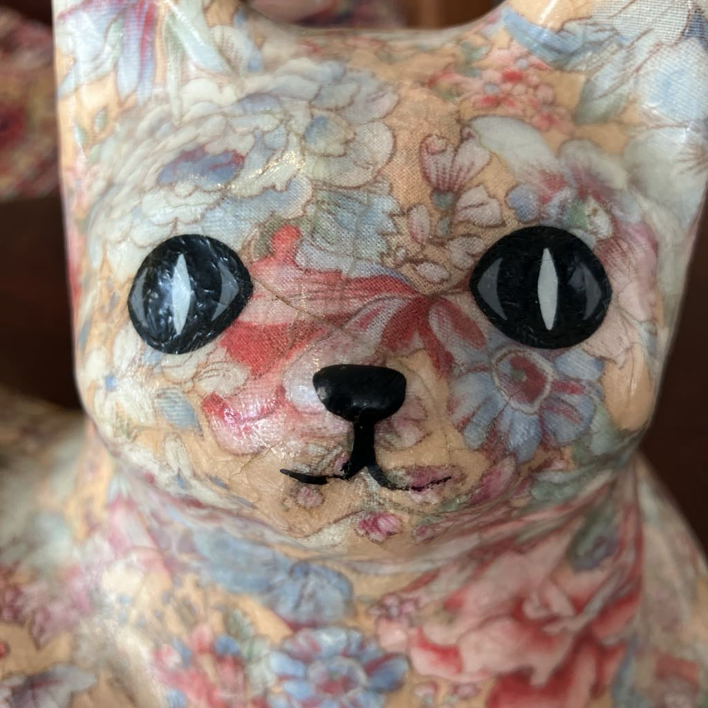 Floral-patterned cat-shaped pillow with black eyes and a black nose.