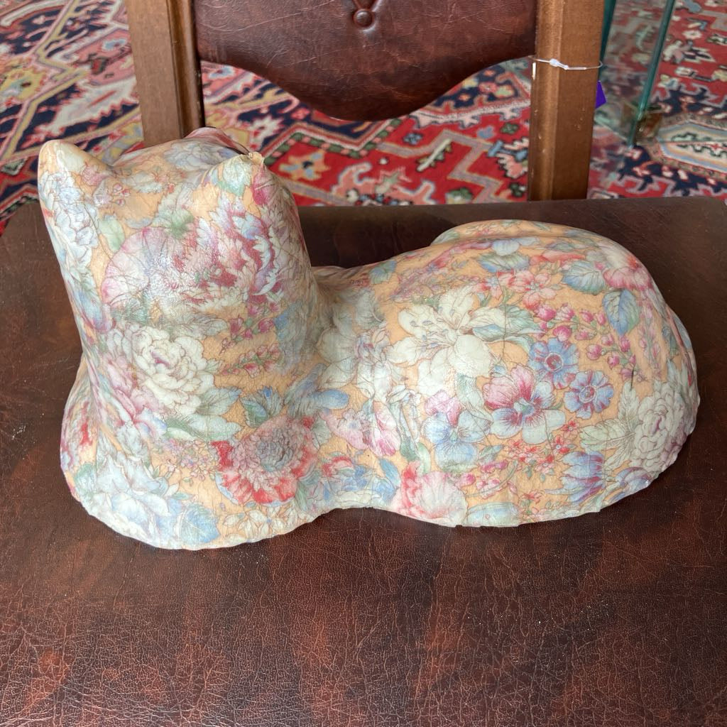Floral-patterned cat-shaped object on a brown leather surface