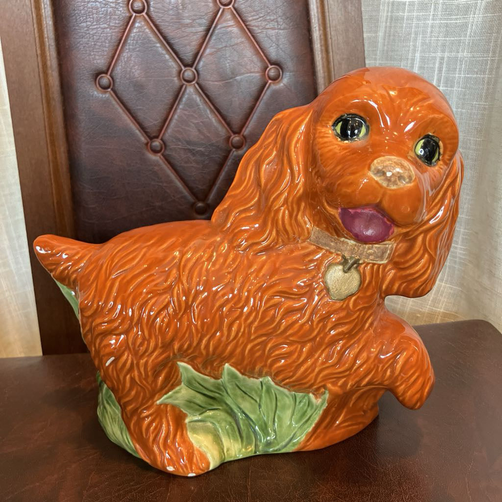Ceramic dog-shaped cookie jar on a wooden surface with a chair in the background.