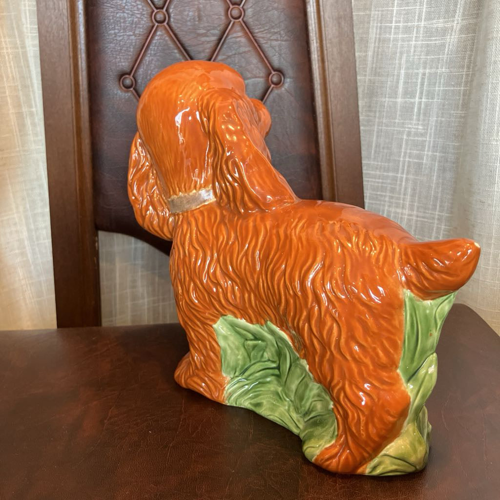 Ceramic dog figurine with a green base on a wooden surface