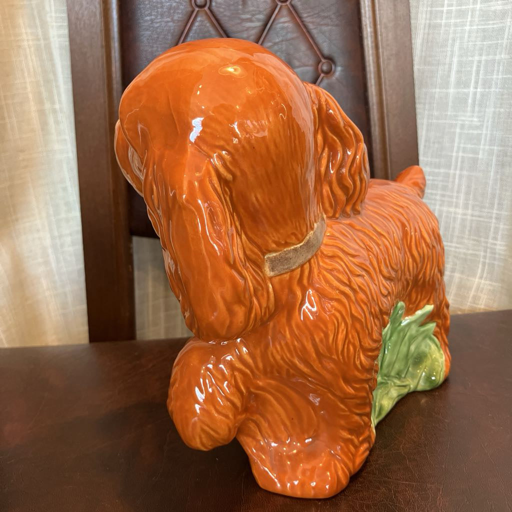 Orange ceramic dog figurine on a wooden surface with a neutral background
