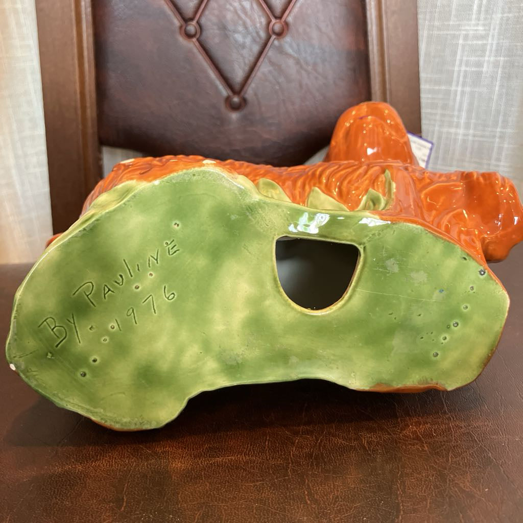 Ceramic dog figurine with 'By Pauline 1976' engraving on a wooden surface.