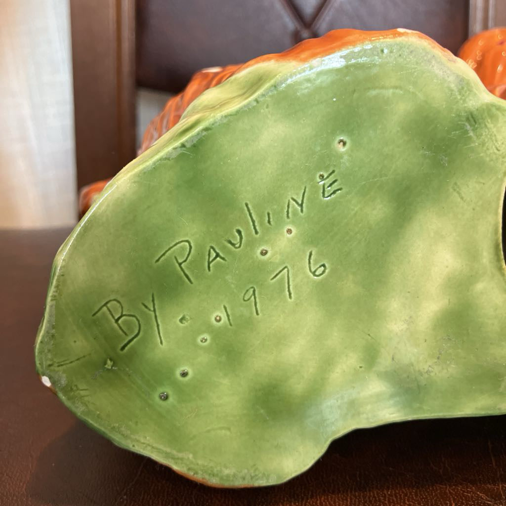 Green ceramic piece with 'By Pauline 1976' inscription on a brown surface