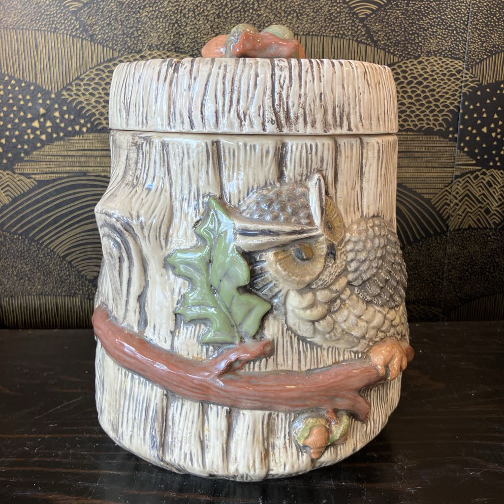Decorative jar with owl and leaf design on a wooden surface