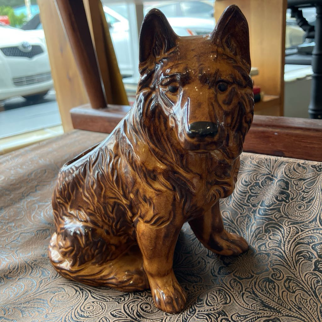 Brown ceramic dog figurine on a patterned surface with a window and car outside.