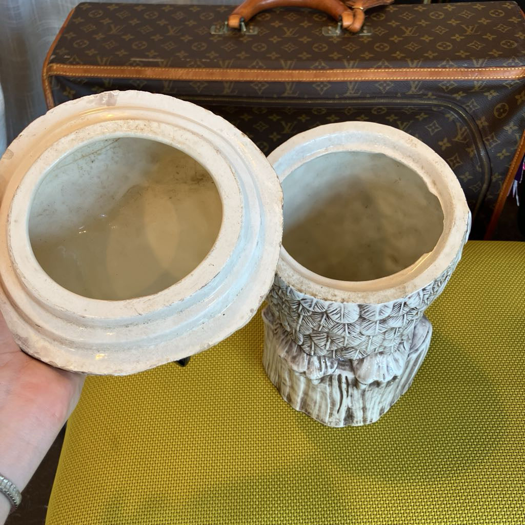 Two ceramic containers with a textured surface, one open, held in front of a patterned suitcase.