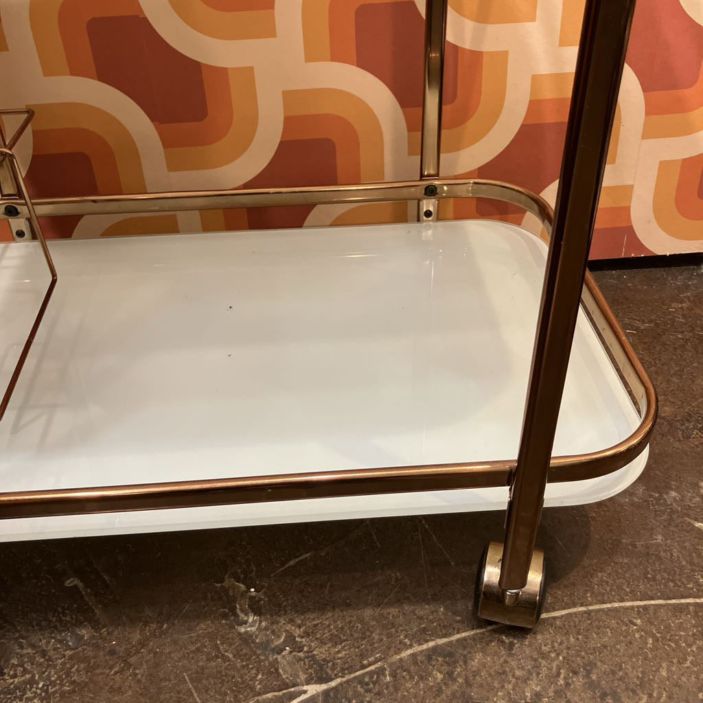 White bar cart with gold accents against a patterned wall.