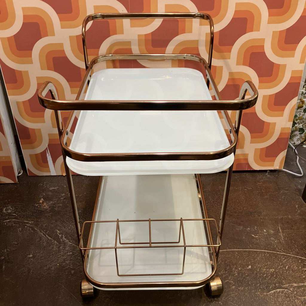 Two-tiered metal serving cart with gold accents against a patterned wall.