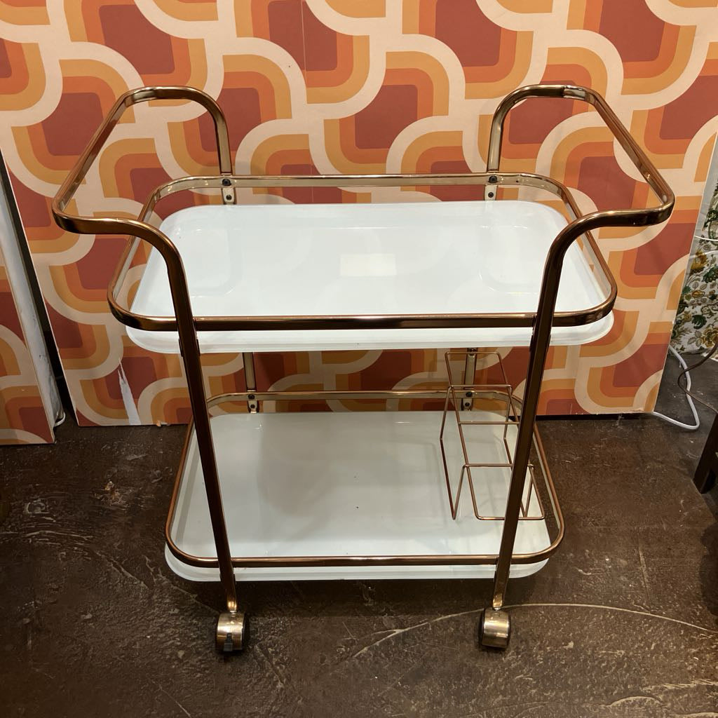 Vintage-style serving cart with gold accents against a patterned wall.