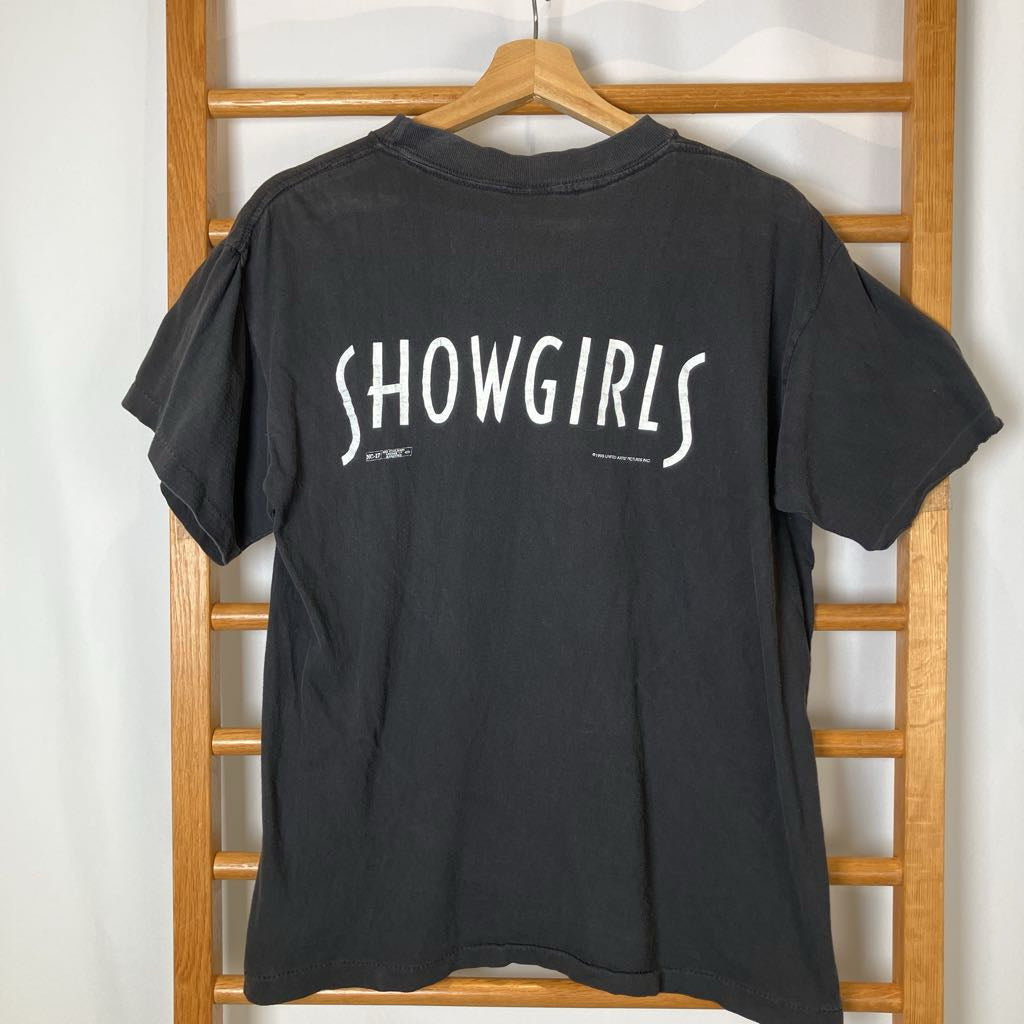 Black t-shirt with 'SHOWGIRLS' text on a wooden rack