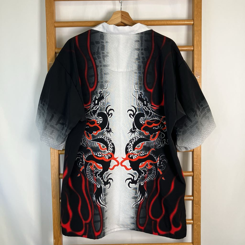 A black kimono-style cardigan with red and gray dragon graphics, hanging on a wooden hanger against a white wall and wooden ladder.