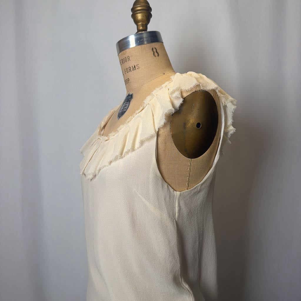 Mannequin wearing a cream-colored garment with a ruffled neckline against a plain background