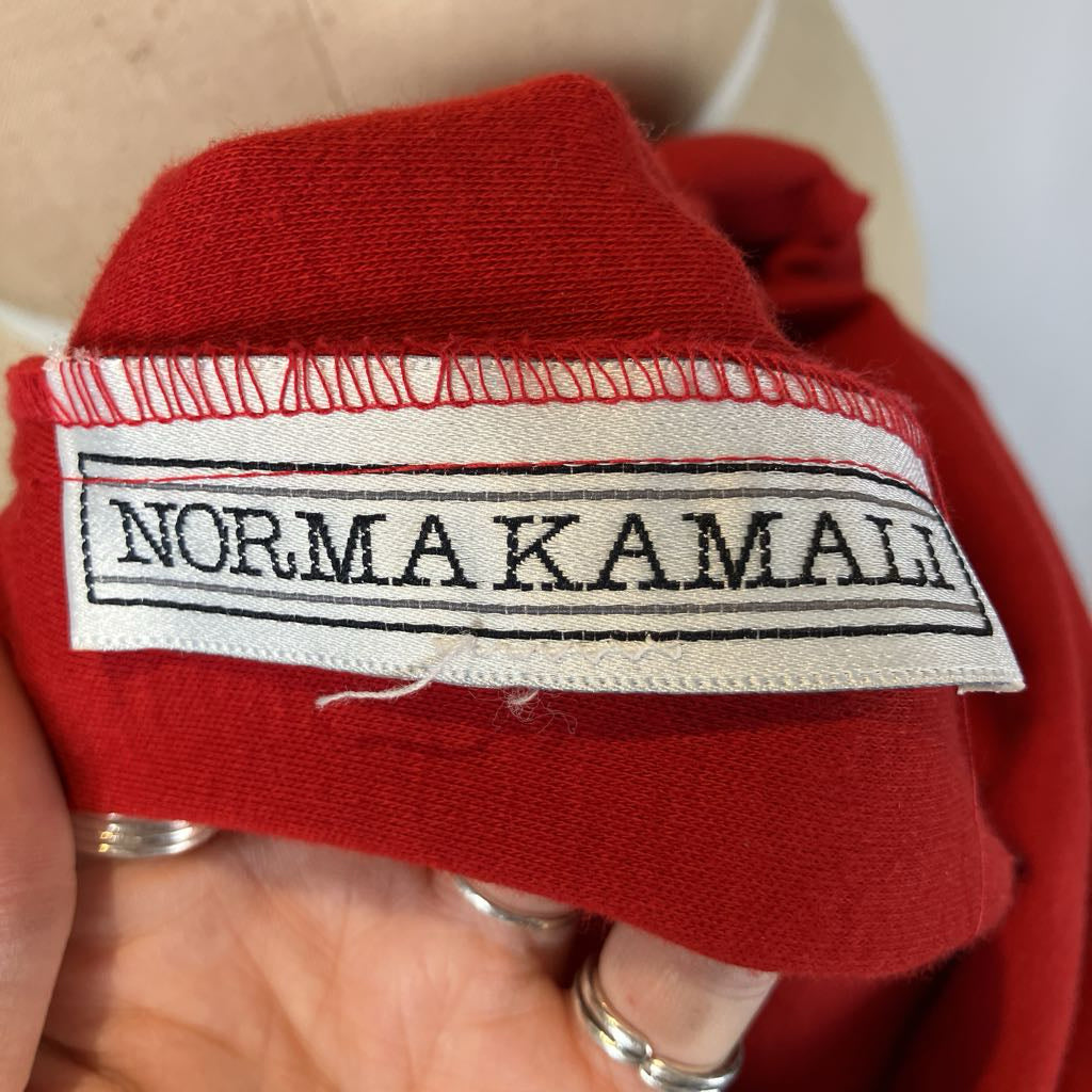 Red fabric with a 'Norma Kamali' label held by a hand.