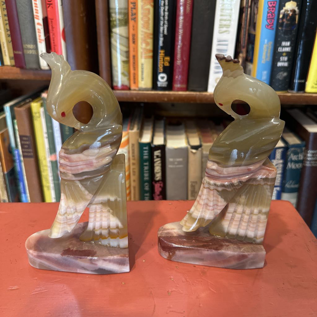 Two stone sculptures of birds on a red surface with a bookshelf in the background.
