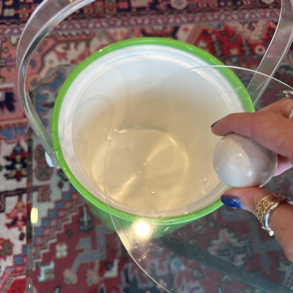 Hand holding a clear container with a green lid on a patterned rug