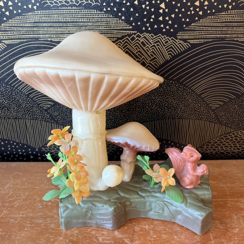 Decorative mushroom figurine with flowers and a small animal on a wooden surface.