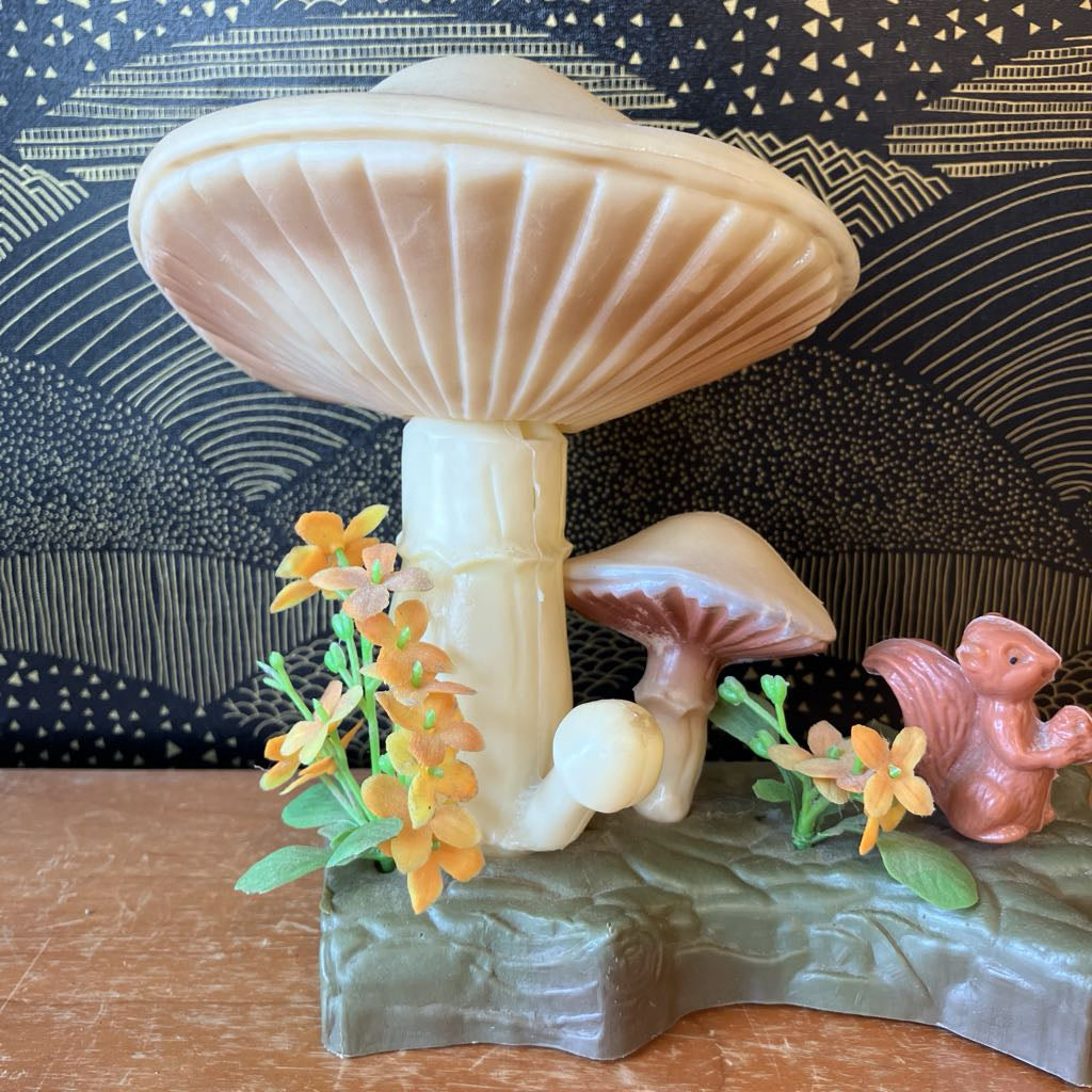 Decorative mushroom sculpture with flowers and a small animal figurine on a wooden surface.
