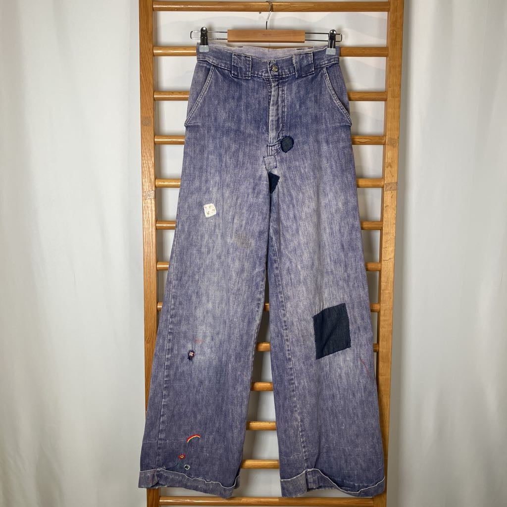 Blue denim jeans with patches on a wooden rack against a white wall